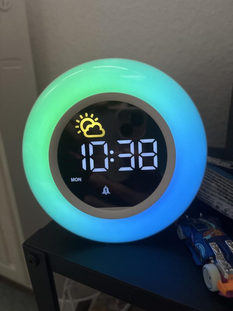 Réveil rond sur fond sombre, affichant l'heure et un icône de météo. Lumière verte et bleue