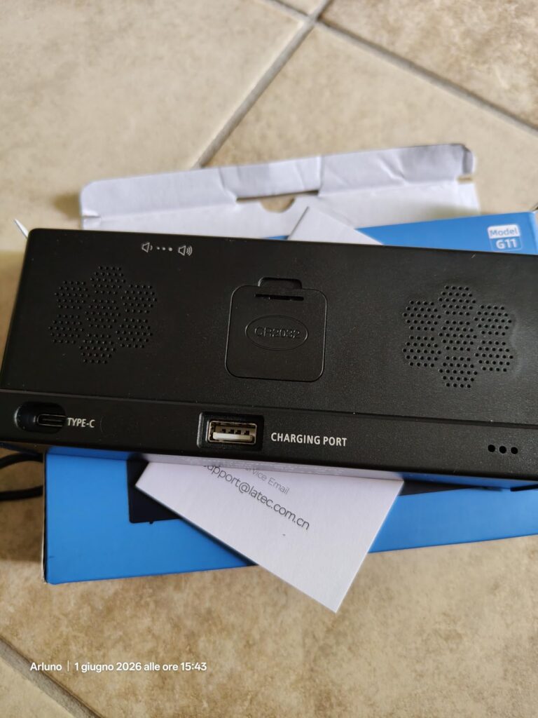 Vue arrière du réveil, sur fond d'emballage, montrant les grilles des haut-parleurs, le compartiment à pile et les ports USB-...
