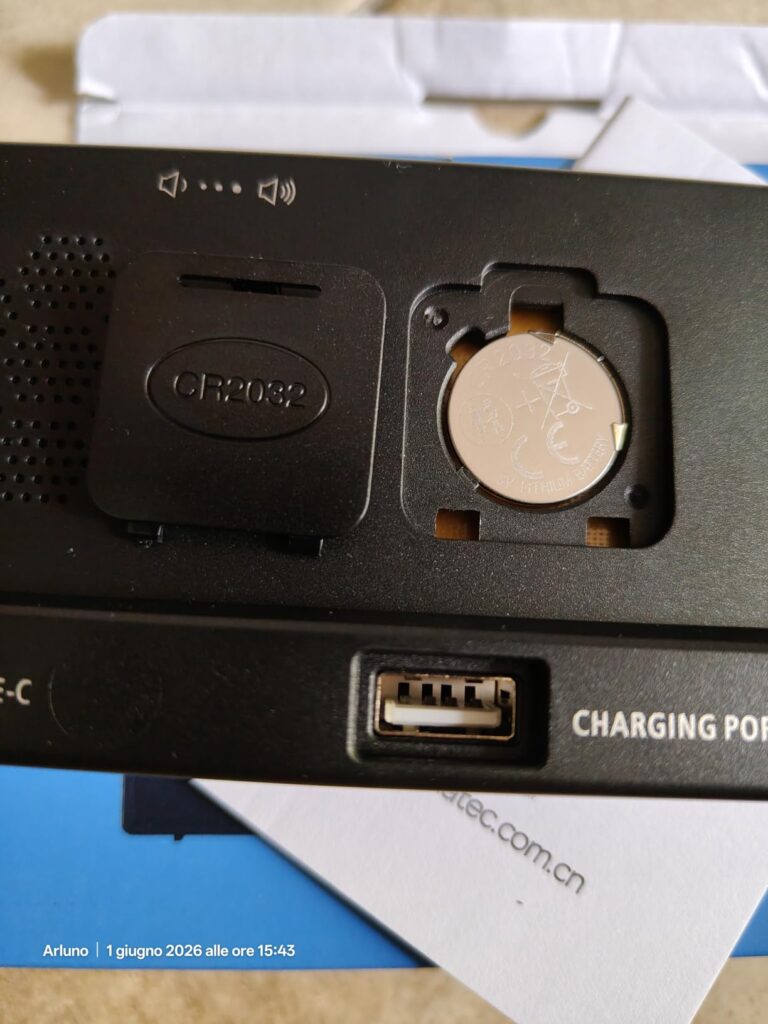 Gros plan sur le dos du réveil, avec le compartiment à pile ouvert et une pile bouton insérée, ainsi que le port USB de charg...