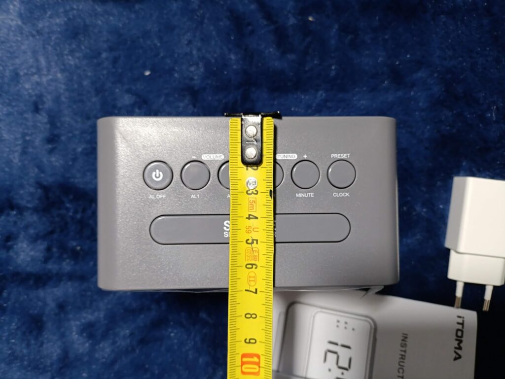 Le réveil est mesuré en hauteur avec un mètre-ruban. Même angle de vue que visuel 1 et 4.