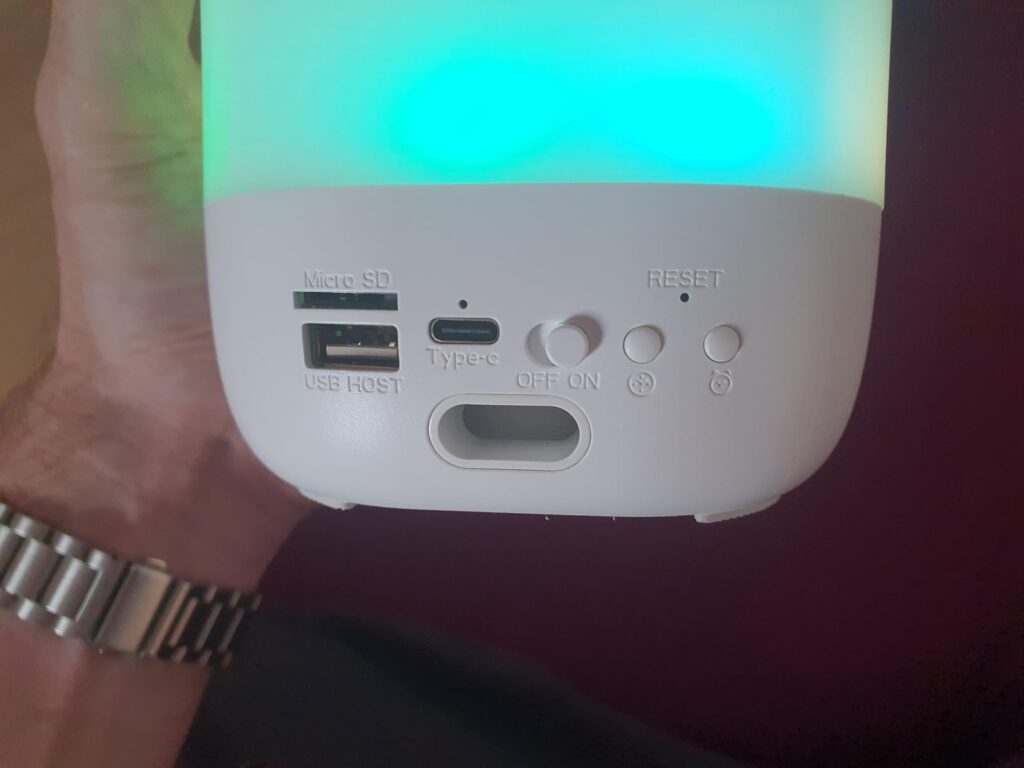 Vue du dessous de l'appareil, montrant les différents ports de connexion et boutons. La lumière de l'appareil est verte/turqu...