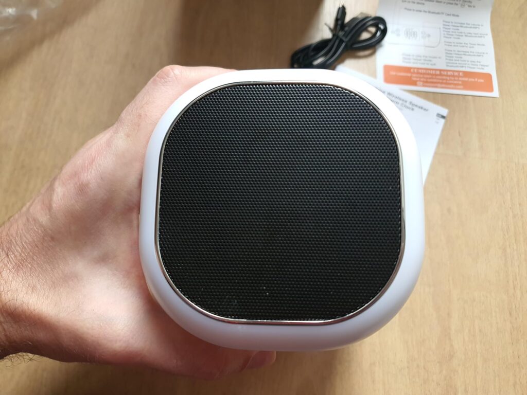 Gros plan sur le dessus de l'appareil, qui est une grille de haut-parleur. Une main tient l'appareil.