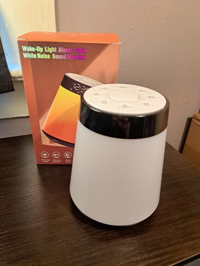 Le réveil lumière avec sa boîte d'emballage. Le produit est sur une table en bois foncé. La boîte est en arrière-plan, légère...