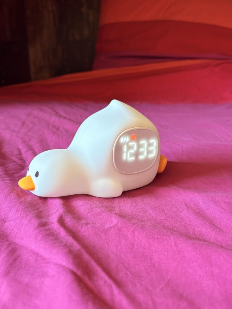 L'oie est posée sur un drap froissé rose avec l'heure 12:33 affichée.