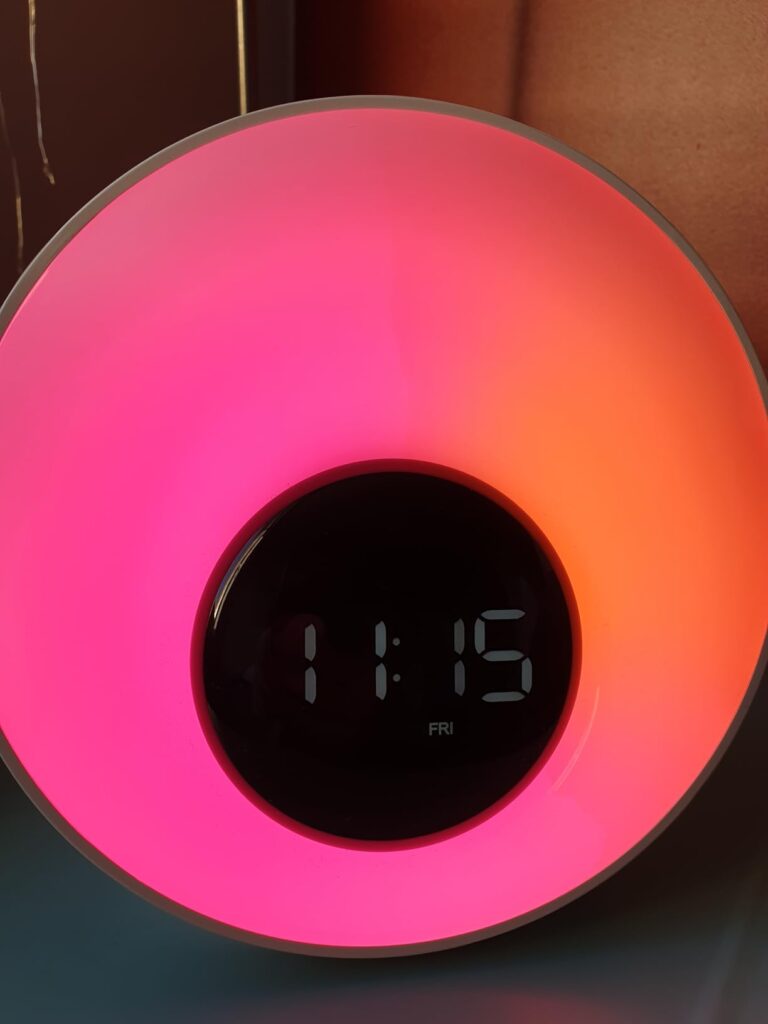 Le réveil lumière sur un fond neutre, avec un éclairage multicolore (rose, orange, jaune).