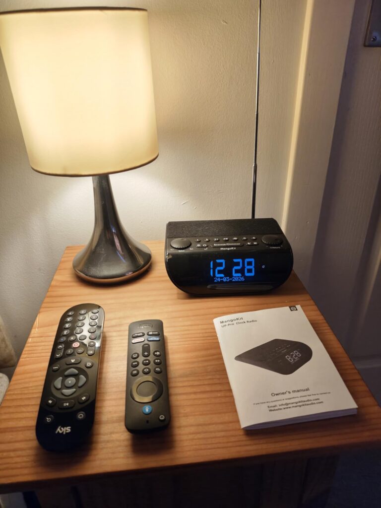 Radio-réveil sur une table de chevet, avec des télécommandes et un manuel
