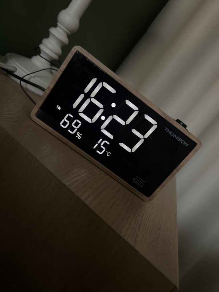 L'horloge sur une table de chevet, avec un éclairage faible, affichant l'heure, l'humidité et la température.