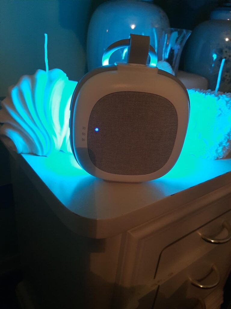 Vue du produit posé sur un meuble avec une lumière bleue et un fond de décorations.