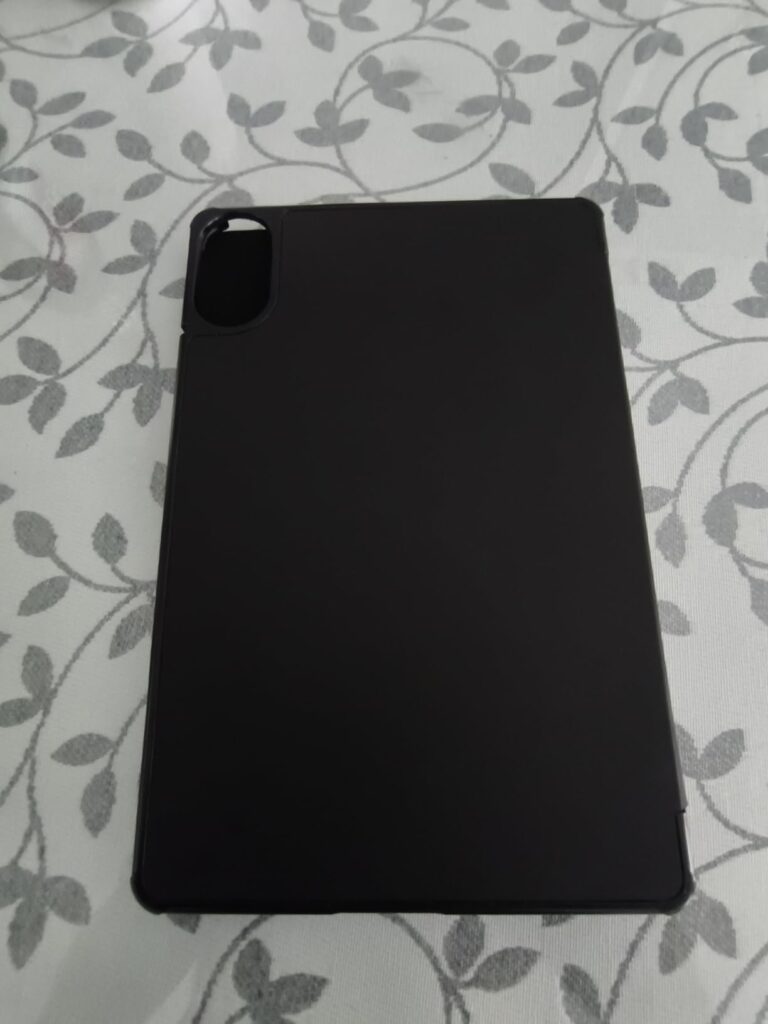 La face arrière de la coque noire d'une tablette, sur un fond en tissu clair à motif végétal. On aperçoit la découpe pour l'a...
