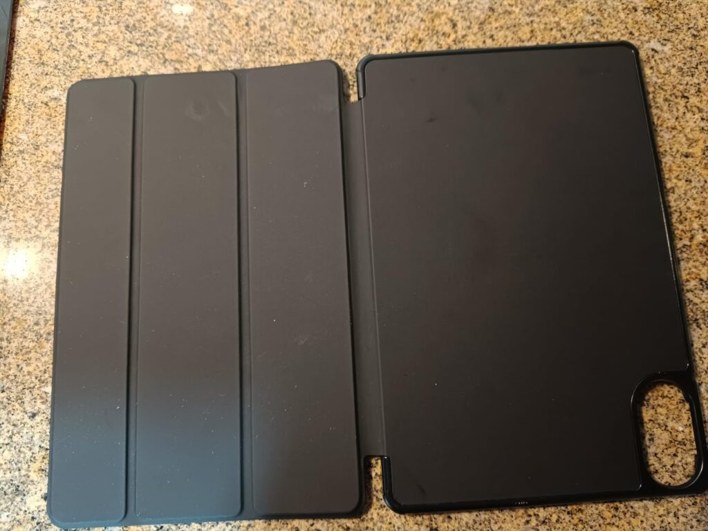 La housse de protection de tablette, ouverte, posée à plat sur une surface marron clair. On voit l'extérieur du couvercle et...
