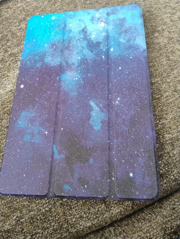 La housse de tablette sur un fond texturé. Le couvercle est décoré d'un motif de galaxie.