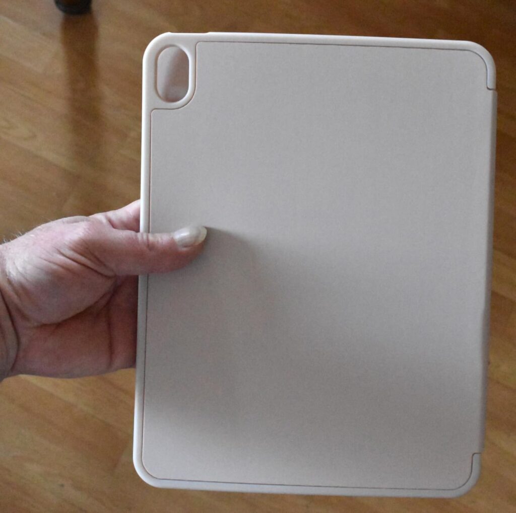 La coque est tenue par une main, montrant le dos de la coque. L'emplacement pour l'appareil photo est visible en haut à gauch...
