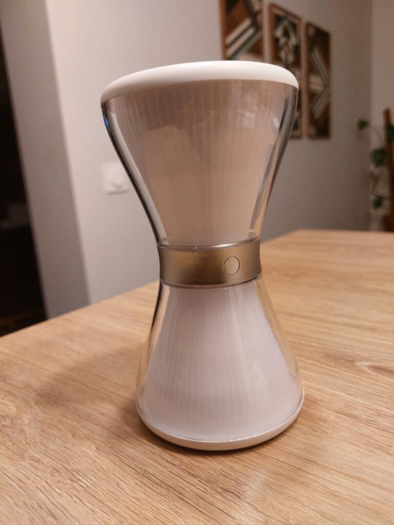Lampe en forme de sablier vue du côté sur une table en bois, le même visuel que le 2 mais d'un angle légèrement différent
