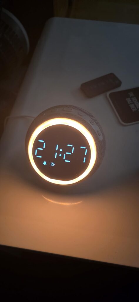 L'enceinte sur une table dans l'obscurité, l'heure 2:17 est affichée avec un anneau lumineux orange.