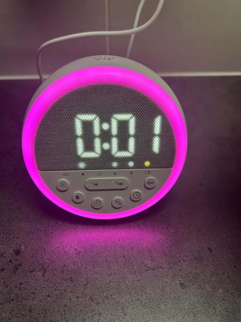 L'horloge LED multifonctionnelle GEMMAC allumée, affichant l'heure 0:01 et une lumière ambiante rose. On voit les boutons de...