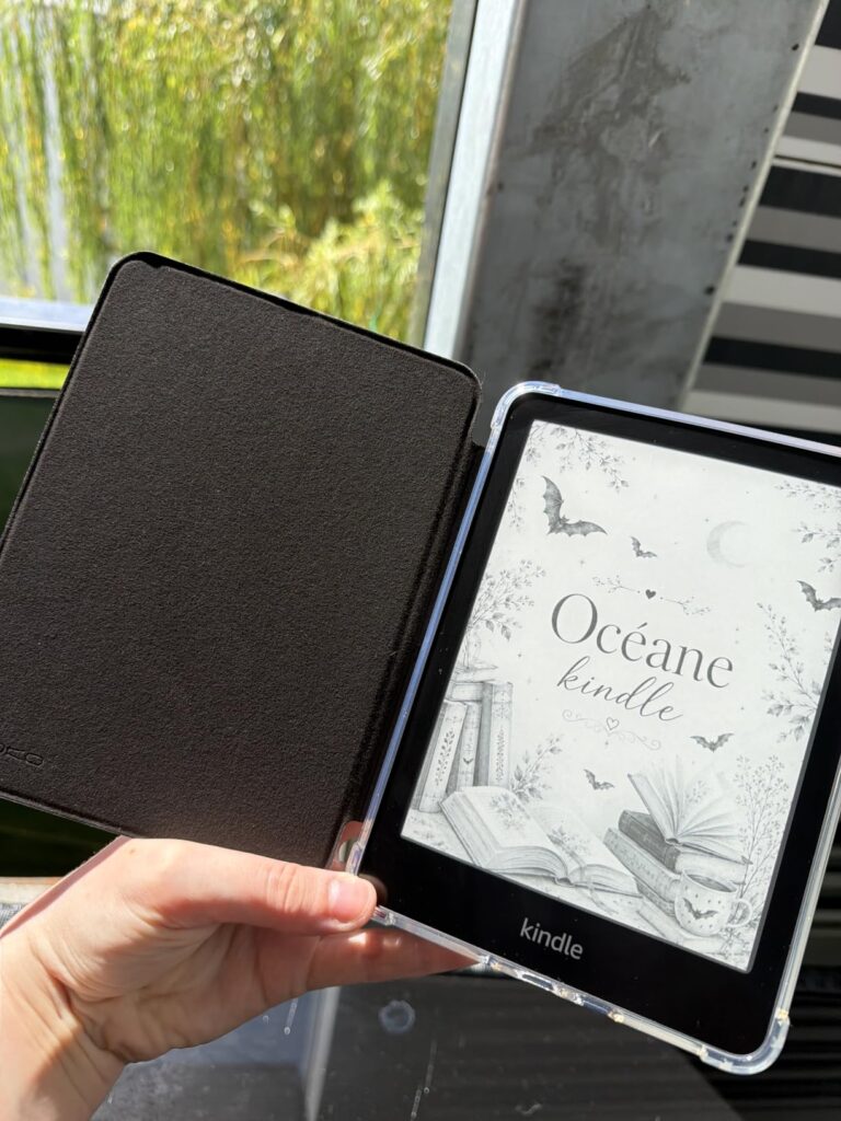 Une liseuse Kindle dans son étui ouvert, tenue dans une main, affichant une couverture de livre avec le titre "Océane".