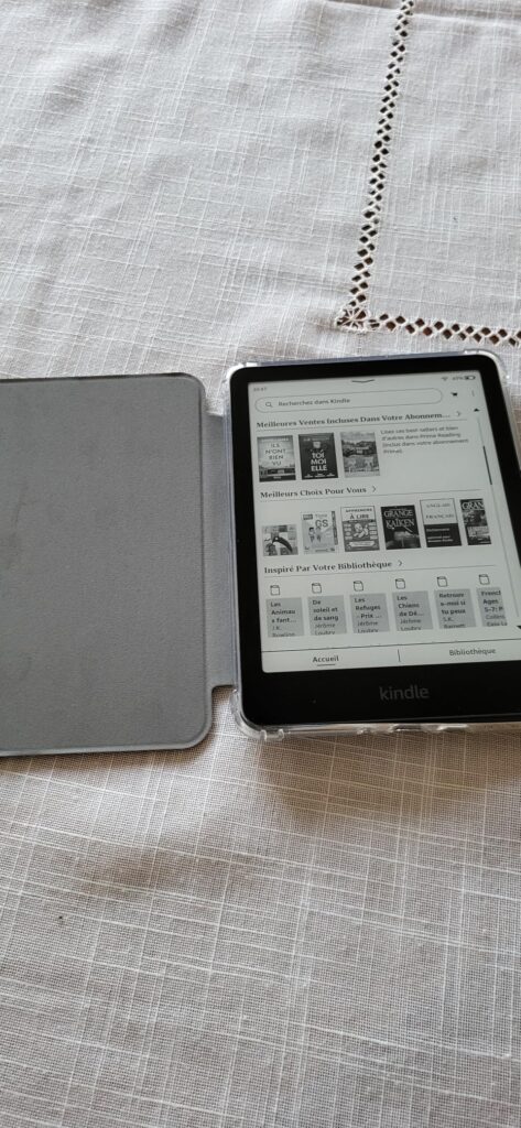 Une liseuse Kindle dans son étui ouvert, posée sur une surface en tissu blanc, affichant la bibliothèque de livres.