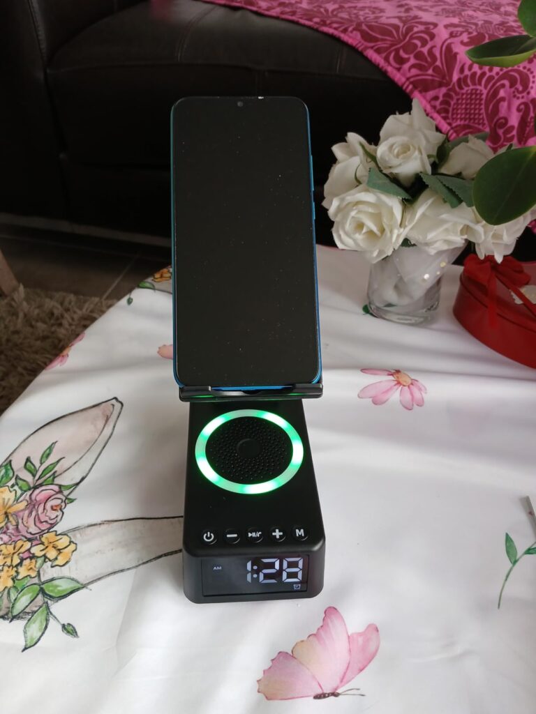 Le produit posé sur une table avec une nappe, un téléphone sur le support. L'éclairage RGB est allumé et l'heure est affichée...