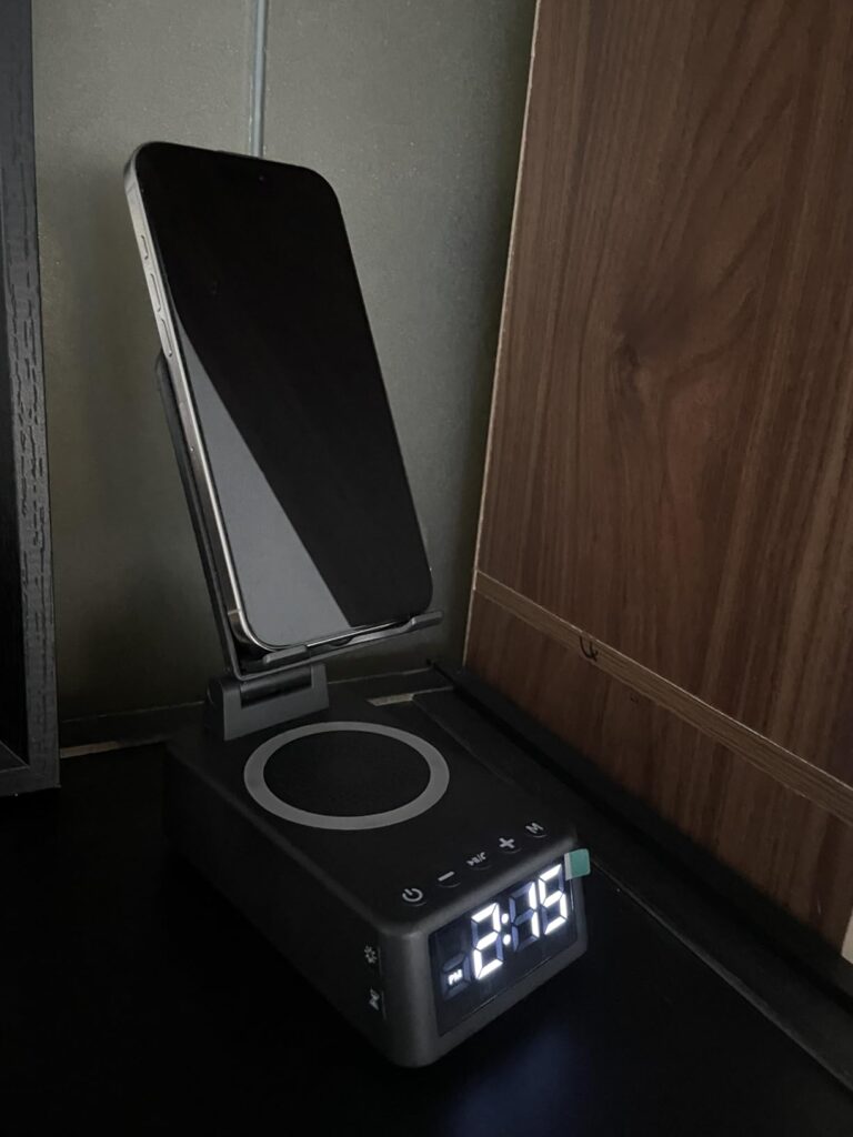 Le produit posé sur une table de chevet, avec un téléphone posé sur le support. L'heure est affichée.