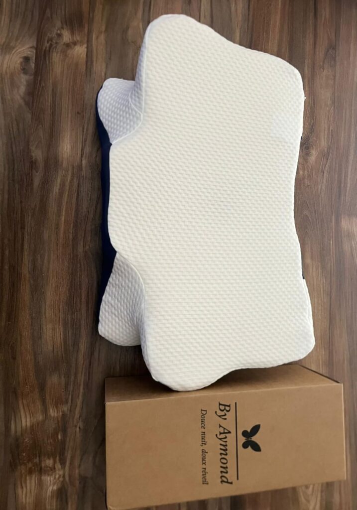 Le coussin By Aymond, vu d'un angle légèrement différent du visuel 0, montrant son côté blanc, avec sa boîte d'emballage en c...