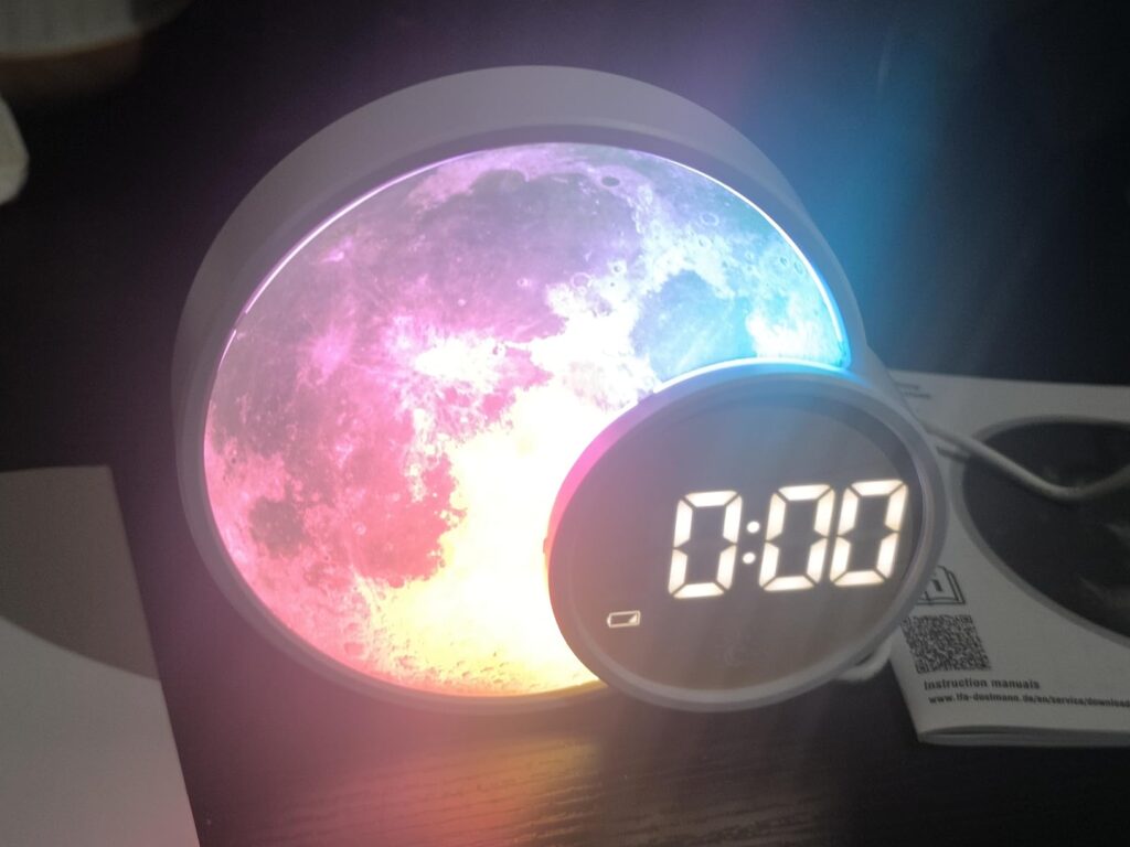 Appareil en marche, affichant l'heure. Vue de face sur un fond noir. L'appareil est posé sur une table noire. Le motif lunair...