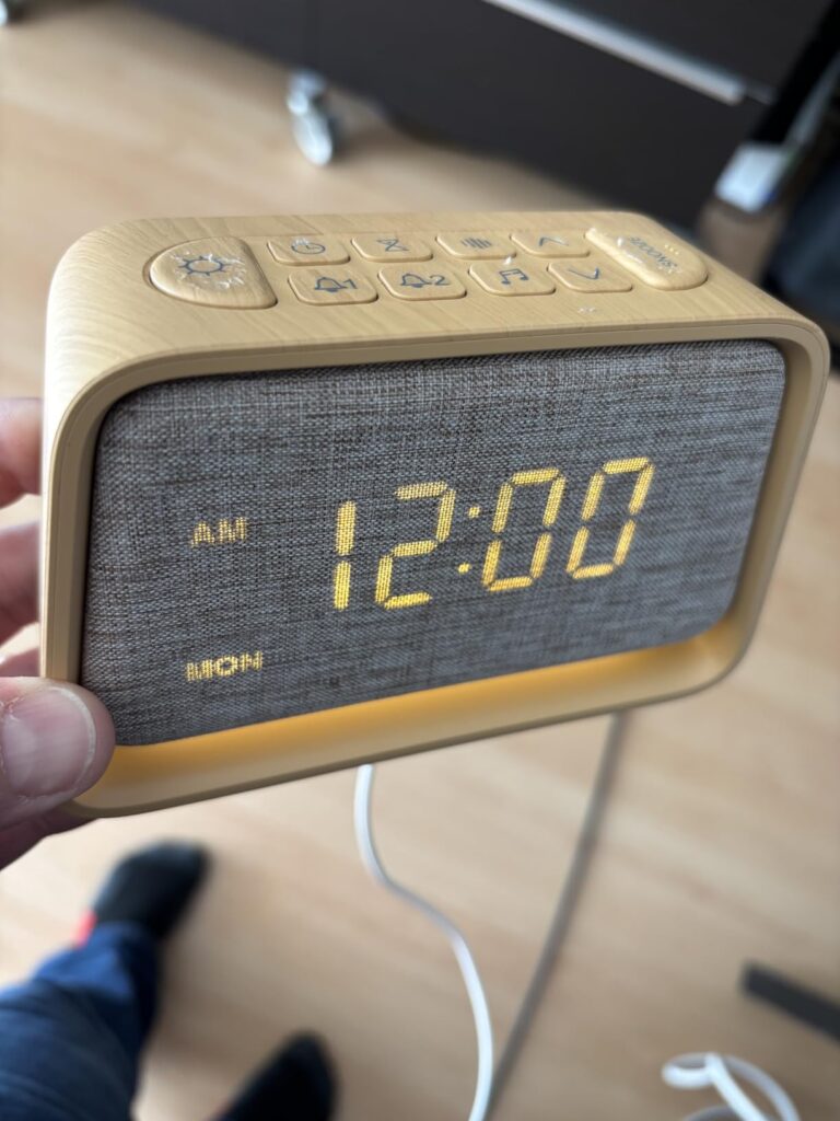 Le radio-réveil vu de dessus, écran allumé, tenu dans une main.