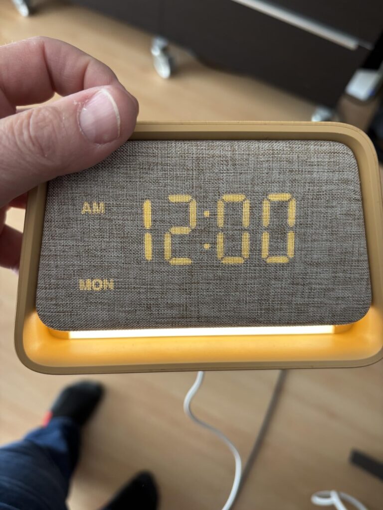 Le radio-réveil vu de face, écran allumé, tenu dans une main.