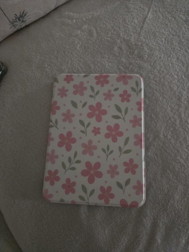 L'étui fermé avec un motif floral rose et blanc, posé sur un tissu gris.