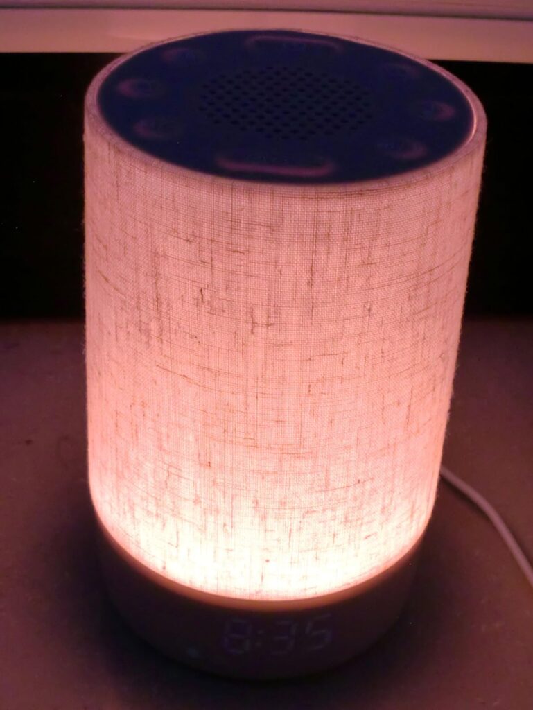 L'appareil allumé, émettant une lumière rose orangé, avec l'heure affichée à sa base.