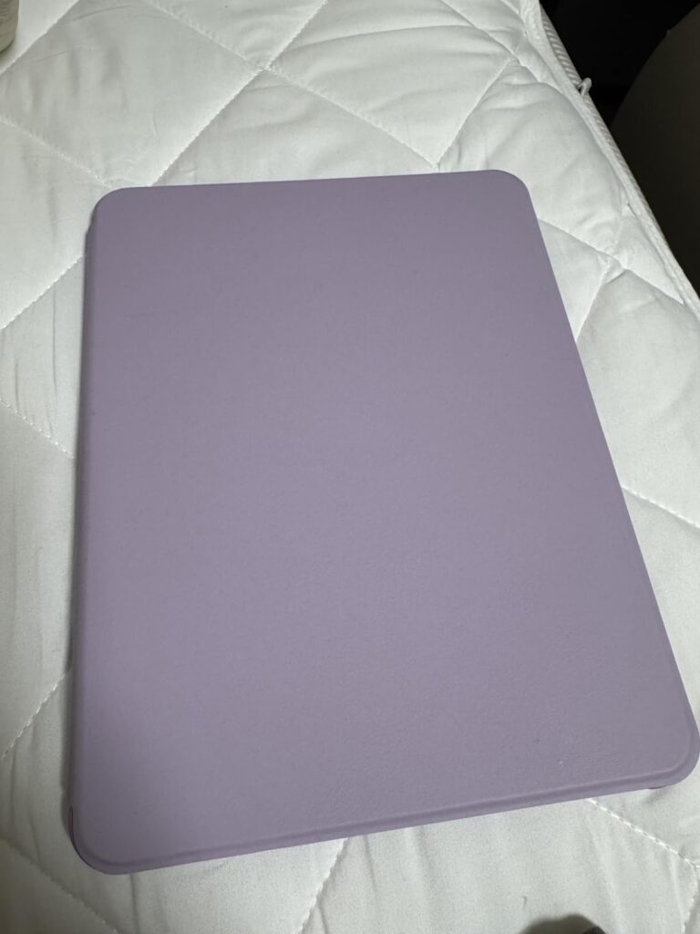 La coque de protection est posée sur un fond clair (un lit avec un drap blanc). La coque est de couleur mauve/violette et est...