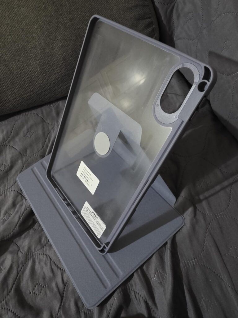 La coque de protection est posée sur un fond sombre (canapé ou plaid). La coque est de couleur mauve/violette et la partie ar...