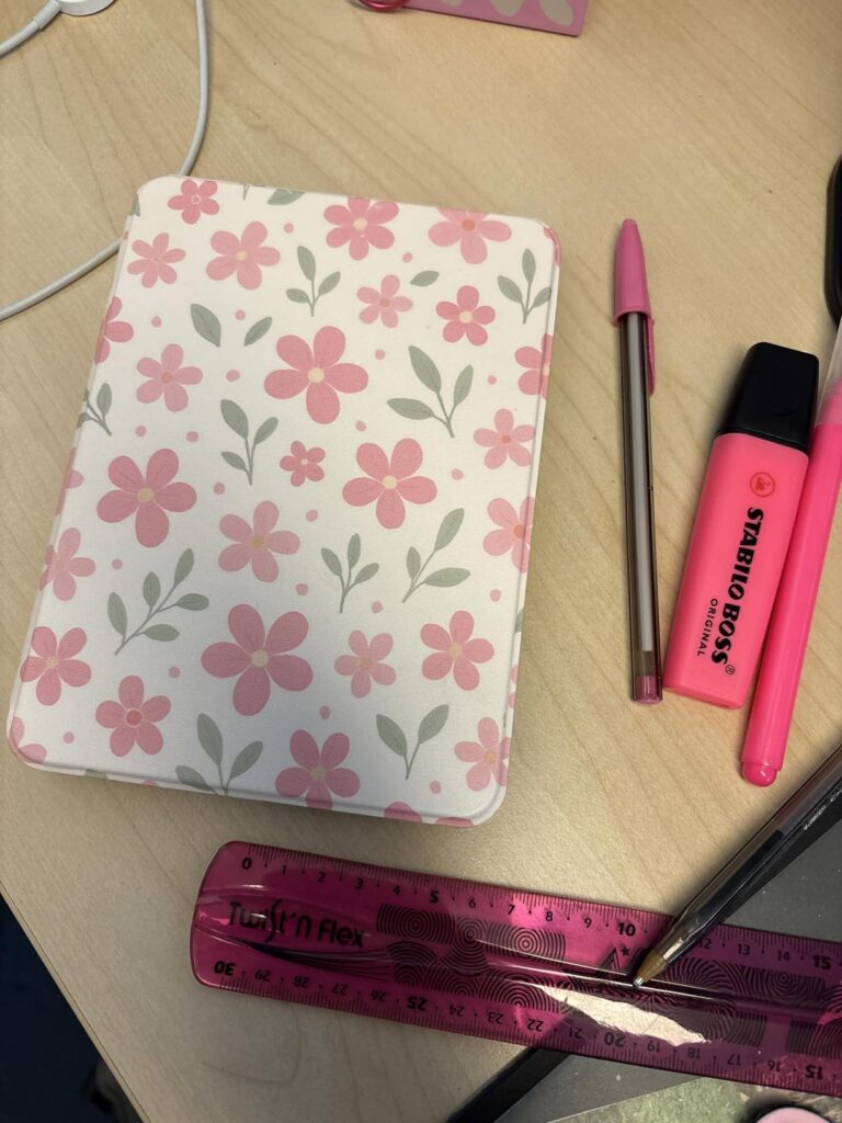 Liseuse fermée posée sur un bureau, couverture à motifs floraux roses. Vue de dessus.