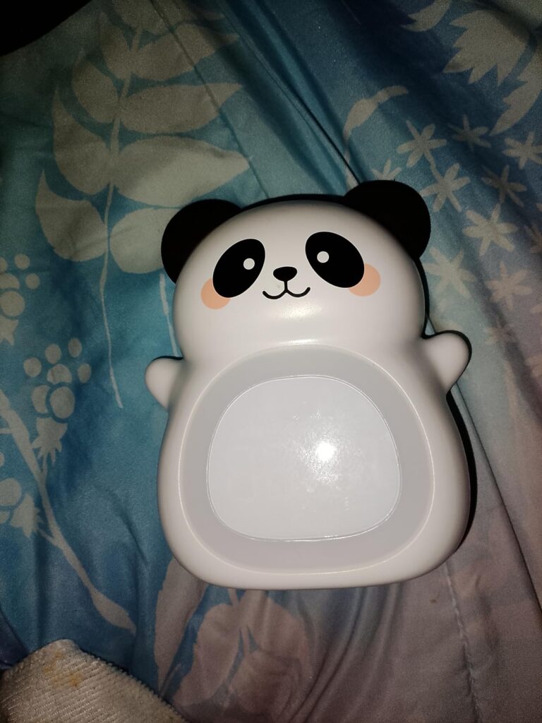 Vue de face du réveil panda éteint, posé sur un tissu bleu à motifs floraux blancs.