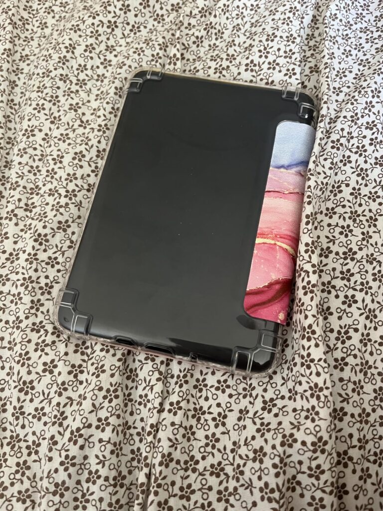Vue arrière de la liseuse Kindle Paperwhite dans sa coque transparente, avec l'étui à motif marbré partiellement visible, pos...