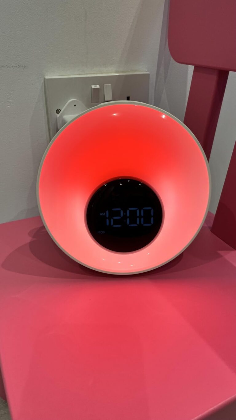 Le réveil lumière sur une chaise rose, affichant l'heure 12:00 et une lumière rouge orangée.