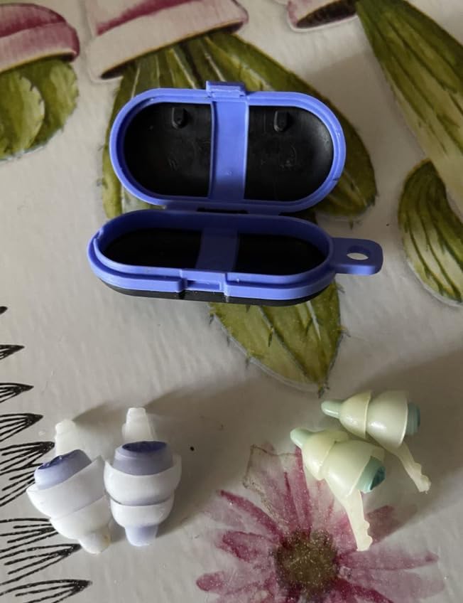 Bouchons d'oreille et leur boîtier de transport bleu ou violet, sur un fond fleuri. Plusieurs paires de bouchons sont posées...