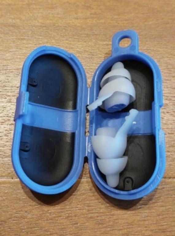 Boîtier de transport bleu pour bouchons d'oreille, ouvert, avec une paire de bouchons à l'intérieur. Le boîtier est posé sur...