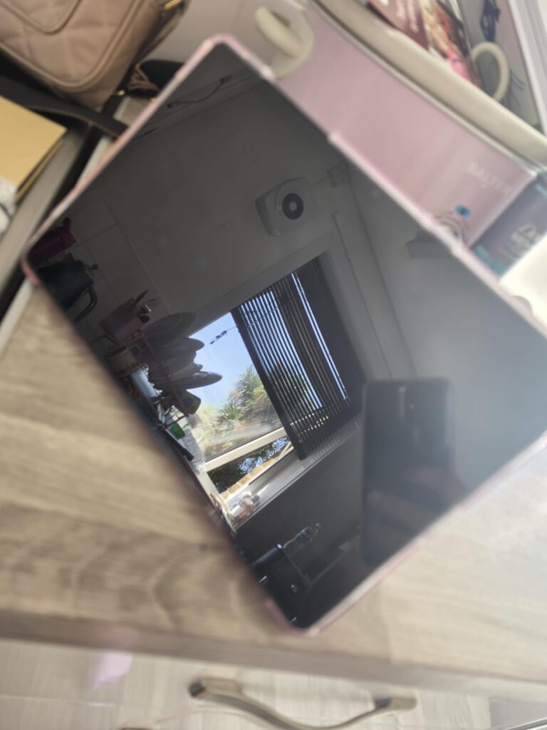 La tablette est posée à plat sur une table, écran noir reflétant l'environnement.