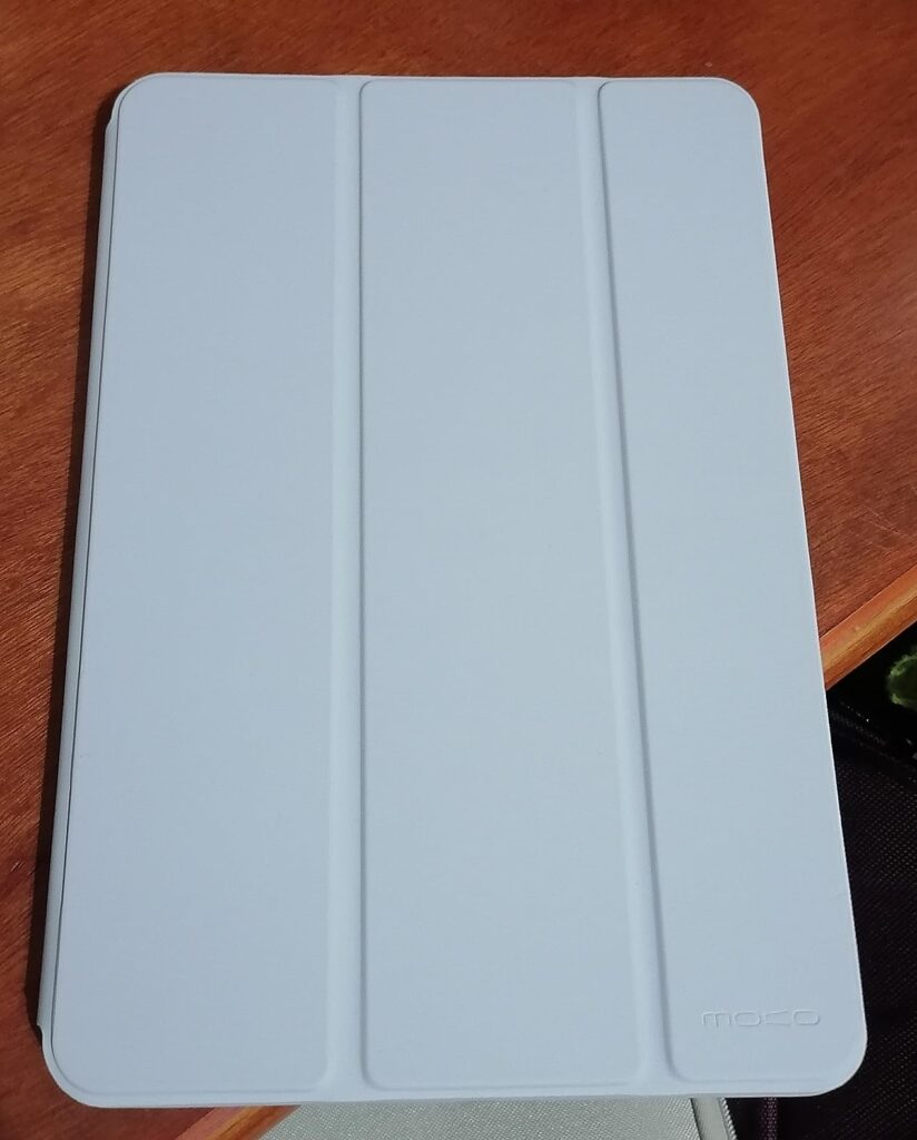 La housse de protection de la tablette, couleur blanche, posée sur une table en bois. On aperçoit un logo dans le coin inféri...