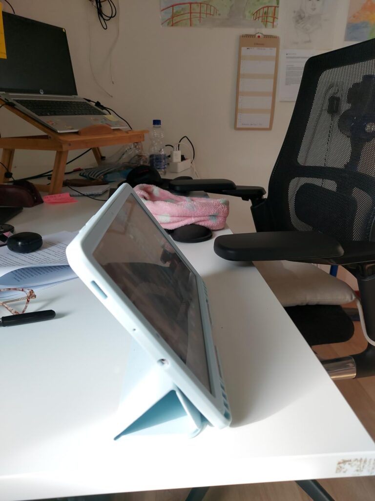 La tablette est posée sur un bureau blanc avec sa housse pliée servant de support, vue de côté. Les images 3 et 4 montrent la...