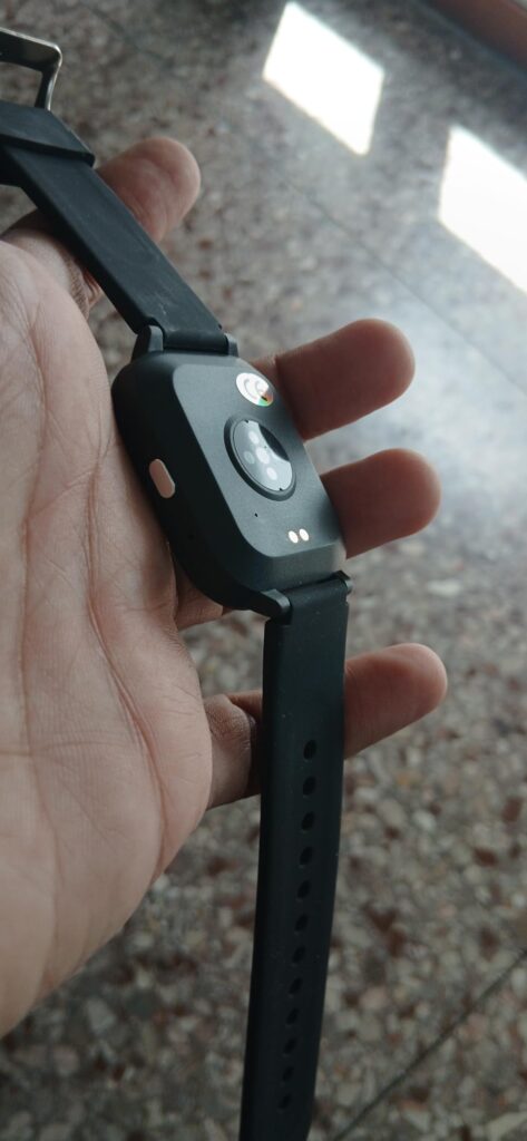 Vue du dos de la montre noire tenue dans une main, montrant les capteurs et le bouton latéral.