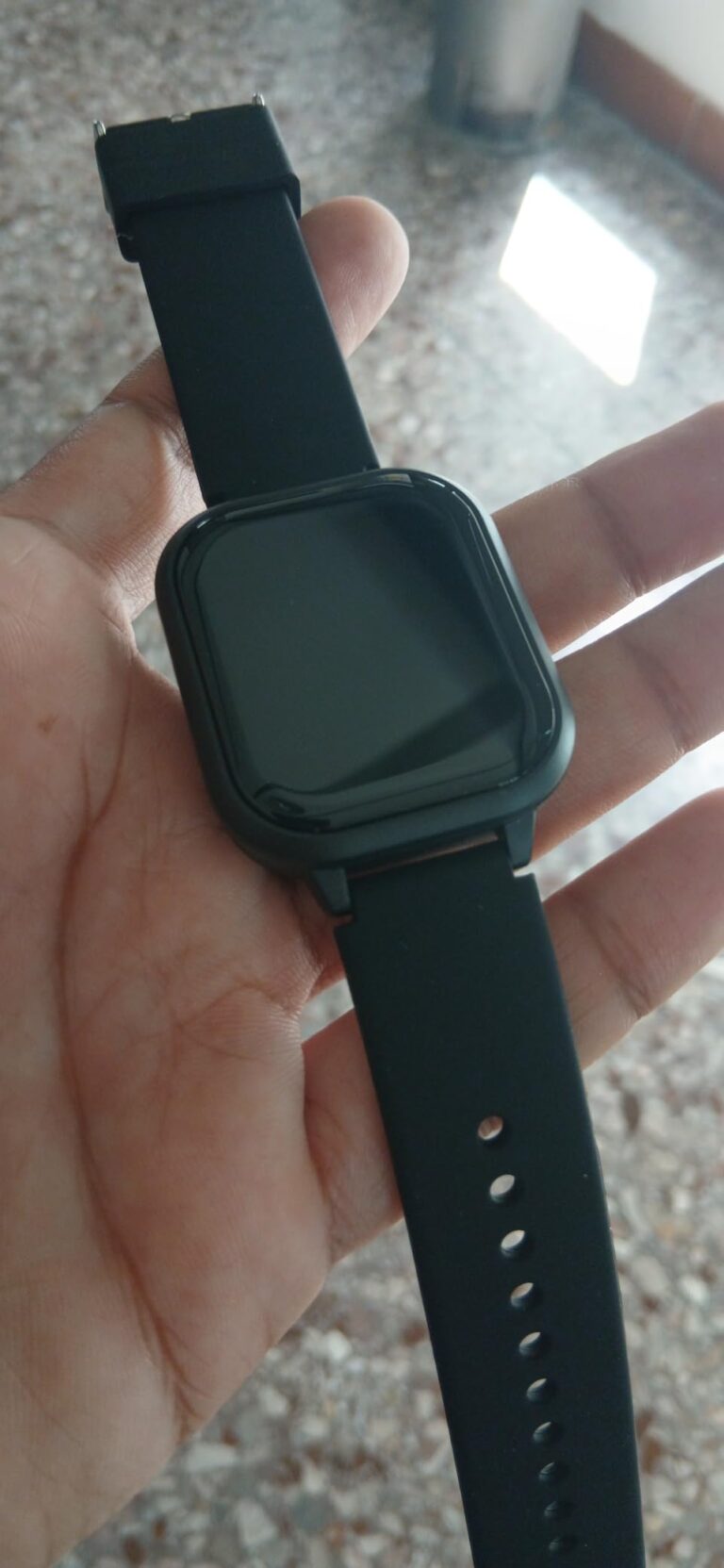 Vue de la montre noire tenue dans une main, écran éteint.