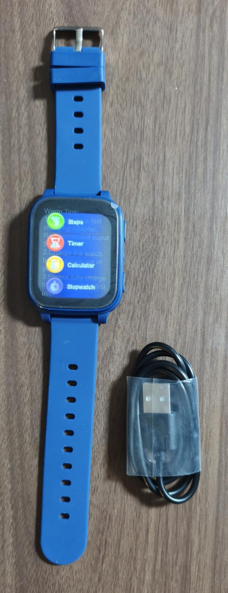 Montre connectée pour enfant avec son câble de chargement, l'écran de la montre affiche des icônes d'applications.