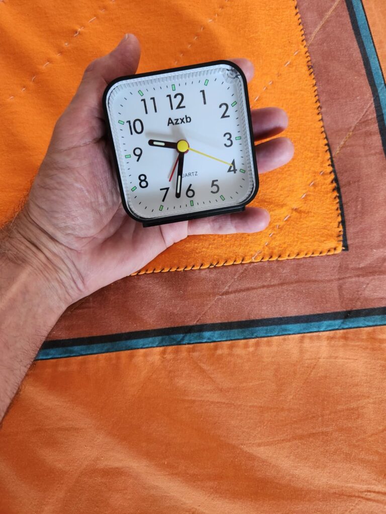 Le réveil tenu à la main, pour montrer sa taille relative, sur un fond orange.