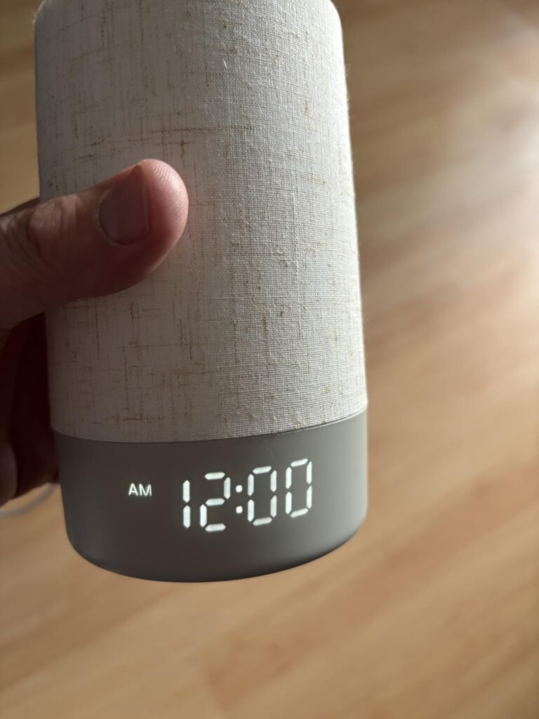 Vue latérale du réveil-enceinte, montrant l'affichage de l'heure. Une main tient l'appareil.