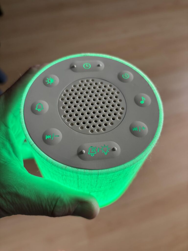 Vue du dessus du réveil-enceinte, l'appareil est éclairé en vert. Une main tient l'appareil.