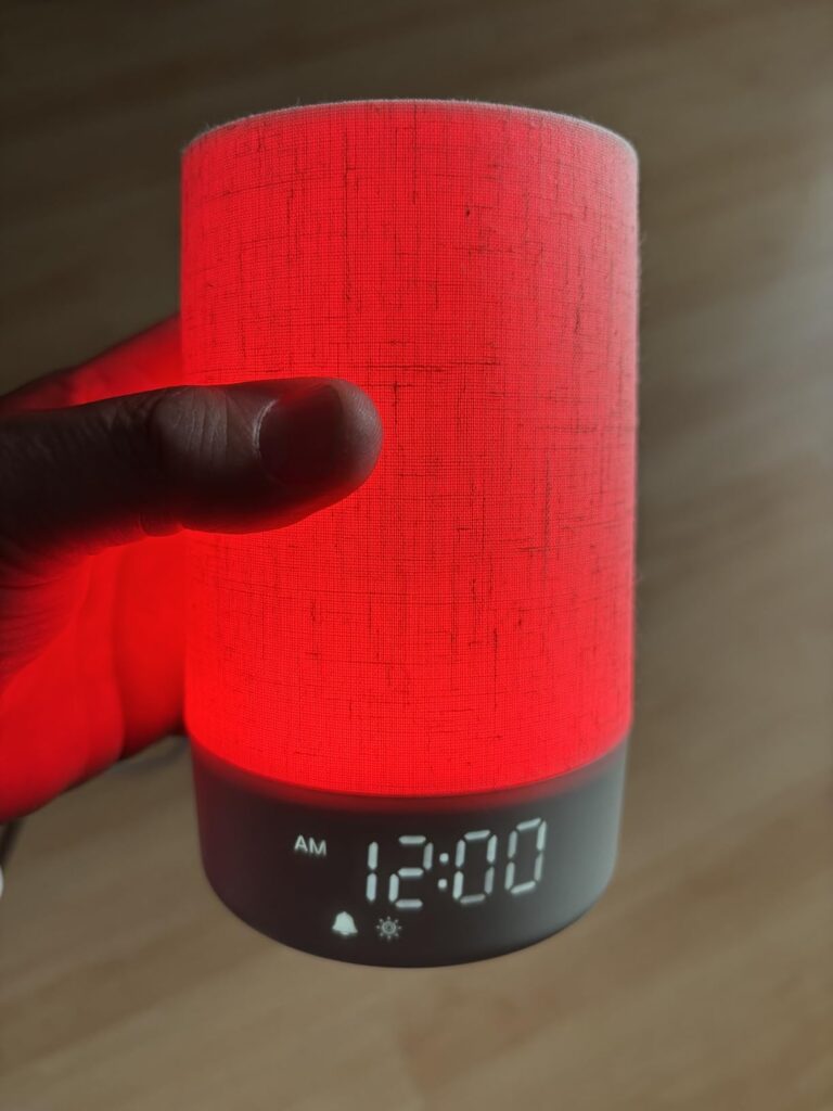 Vue latérale du réveil-enceinte, l'appareil est éclairé en rouge et l'heure est affichée. Une main tient l'appareil.