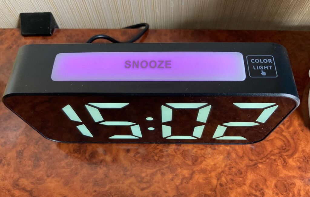 Le réveil sur une commode, avec le bouton 'SNOOZE' allumé en rose et l'heure affichée.