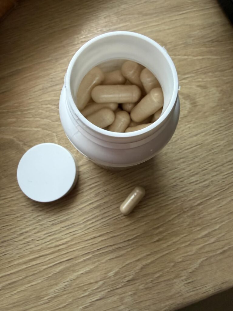 Un flacon de compléments alimentaires ouvert, avec le couvercle à côté et une capsule posée sur la table